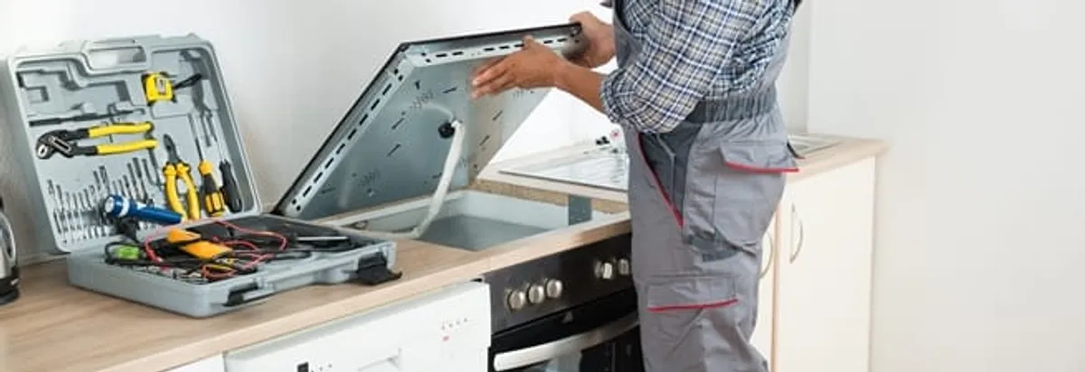 Cooktop repair technician lifting a built-in stovetop for service in Austin, TX