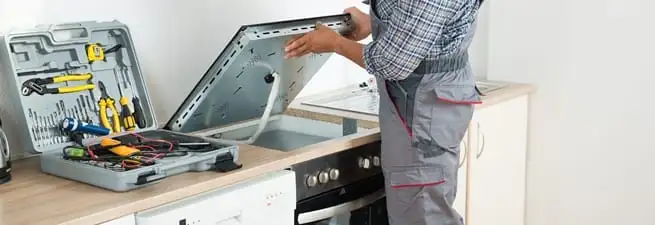 Cooktop repair technician lifting a built-in stovetop for service in Austin, TX