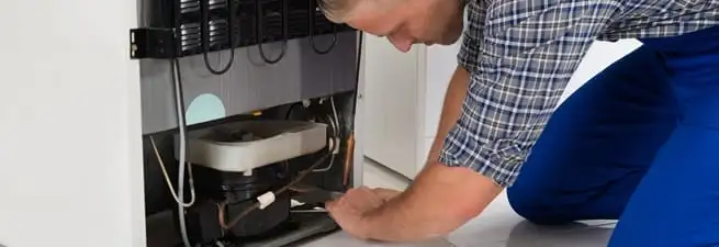 Refrigerator repair technician servicing the compressor and condenser area in Austin, TX