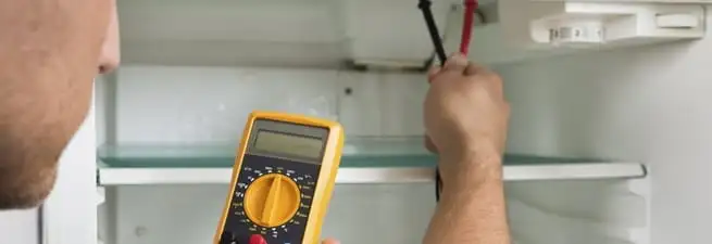Refrigerator repair technician testing electrical components with a multimeter in Austin, TX